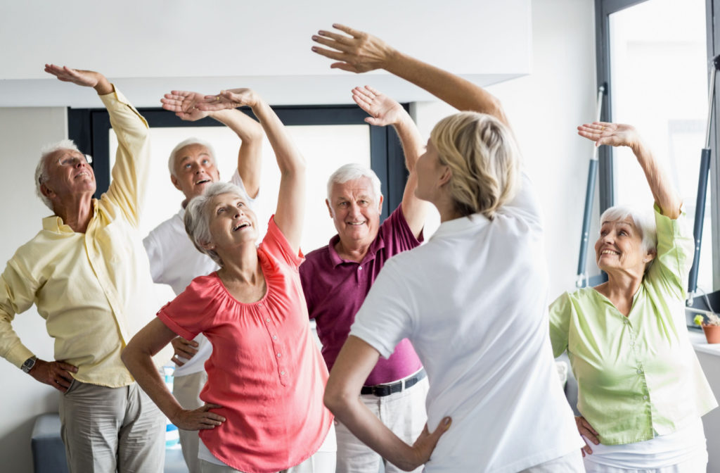 Group of seniors doing exercises, right hand on their waist and stretching their left hand in the air going right.