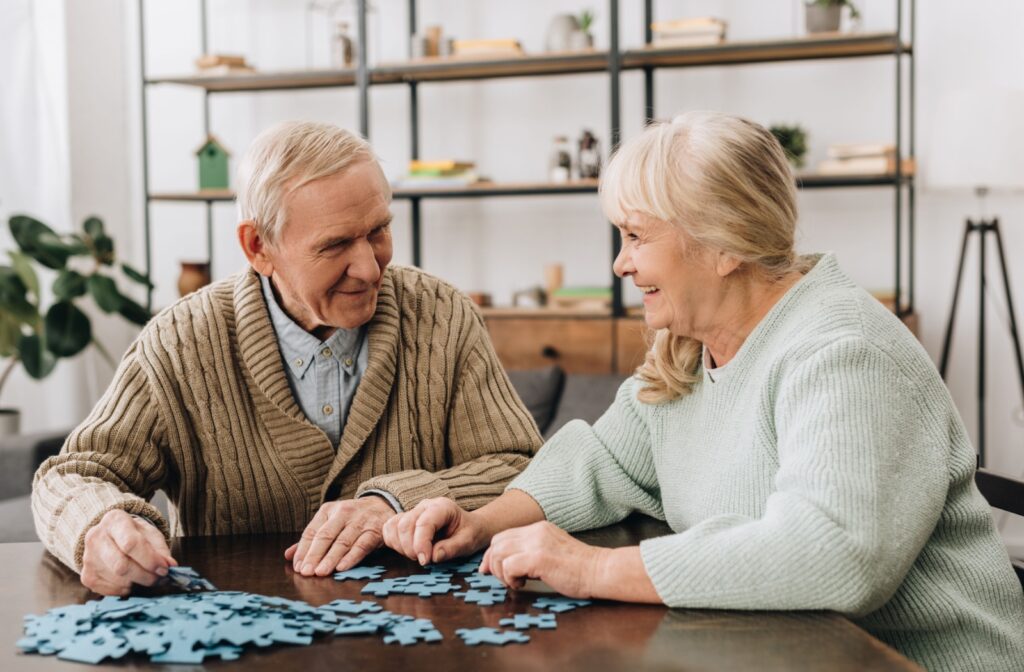 An older man and woman smiling while working on a puzzle together.